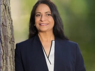 Mona Signh smiling while leaning on a tree outside.