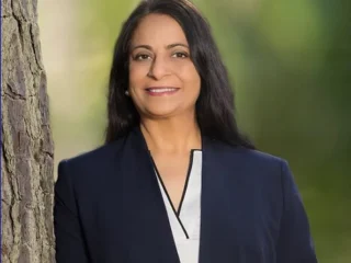 Mona Signh smiling while leaning on a tree outside.
