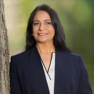 Mona Signh smiling while leaning on a tree outside.