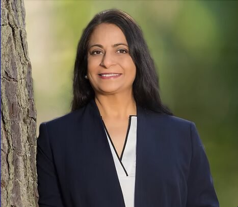Mona Signh smiling while leaning on a tree outside.