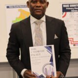 Robert Mitchener in a suit holding a book.