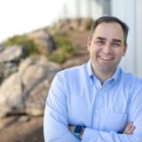 Wiley Nickel smiling and leaning against a wall outside.